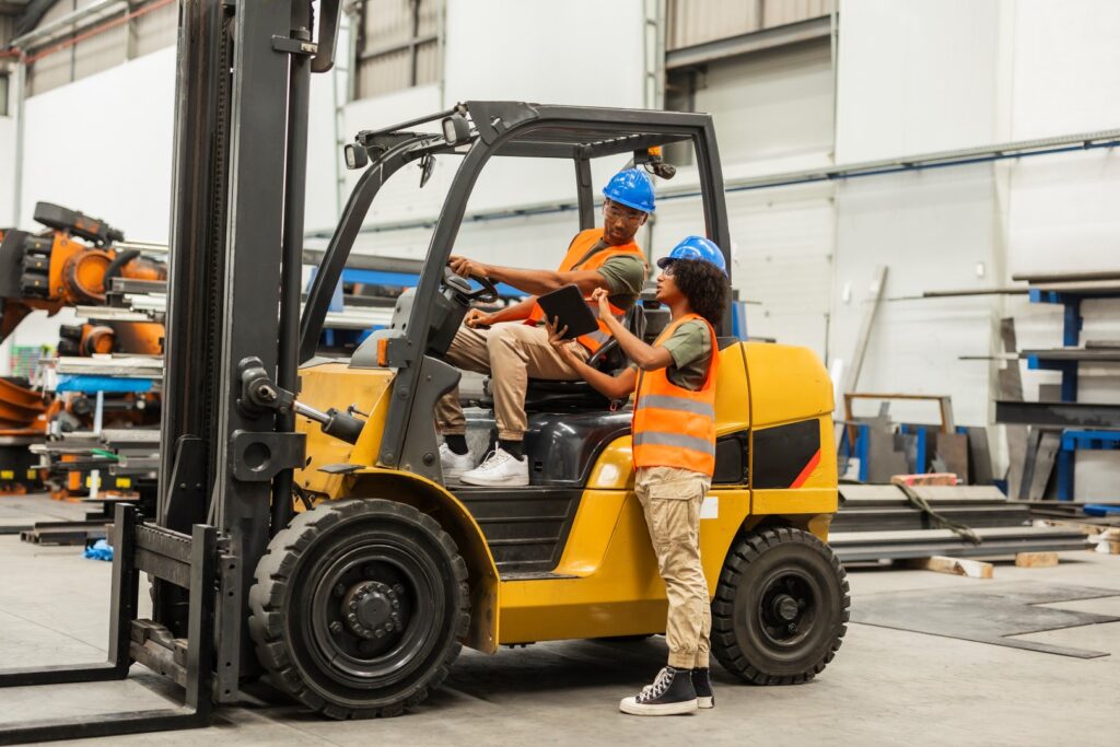 Engineers using digital tablet and driving forklift in factory