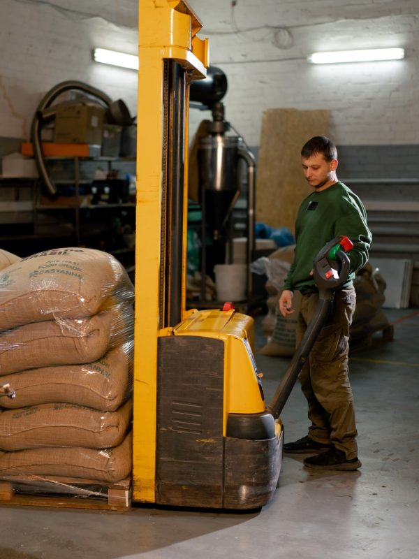 a worker at a coffee factory uses a yellow forklift to lower bags of coffee