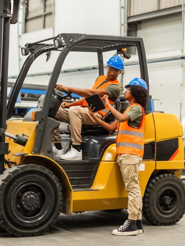 Engineers using digital tablet and driving forklift in factory